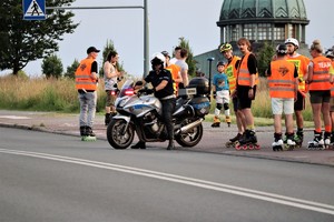 na zdjęciu policjant na motocyklu oraz osoby jadące na rolkach