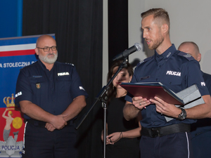 Na zdjęciu umundurowani policjanci, jeden z nich przemawia do mikrofonu