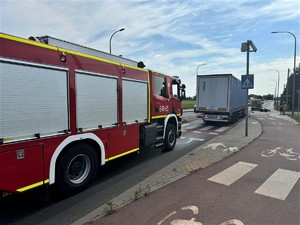 Na zdjęciu wóz straży pożarnej. W tle motocykl przewrócony na bok, karetka oraz inne samochody jadące drogą.