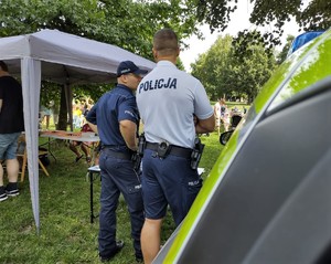 Na zdjęciu umundurowani policjanci stojący obok radiowozu.