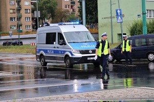 Na zdjęciu policjant z ruchu drogowego oraz radiowóz na skrzyżowaniu.