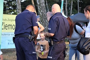 Na zdjęciu umundurowani policjanci wręczający chłopcu kolorowankę i odblask.