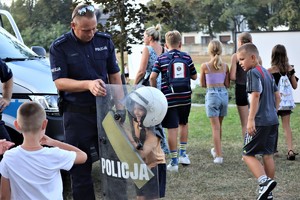 Na zdjęciu umundurowany policjant zakładający chłopcu kask.