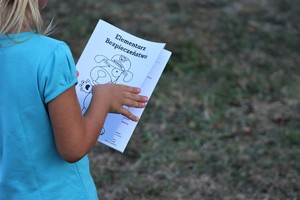 Na zdjęciu dziewczynka stojąca tyłem, trzymająca książeczkę z rysunkiem Sznupka. Na książeczce napis o treści: Elementarz bezpieczeństwa.