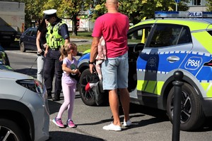 Na zdjęciu umundurowany policjant oraz mężczyzna z dziewczynką obok radiowozu.