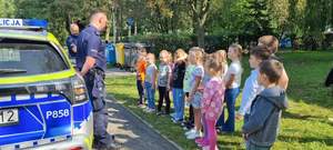 Na zdjęciu umundurowany policjant  z dziećmi przy radiowozie.