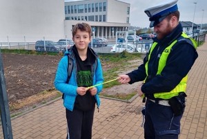 Na zdjęciu  umundurowany policjant wręczający odblask chłopcowi.