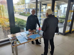 Na zdjęciu umundurowany policjant oraz mężczyzna przy stanowisku Komendy Miejskiej Policji w Tychach w Zakładzie Ubezpieczeń Społecznych w Tychach.