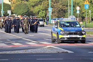 Na zdjęciu oznakowany radiowóz. Za nim orkiestra oraz uczestnicy przemarszu.