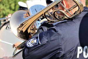 Na zdjęciu stojący tyłem policjant z orkiestry grający na instumencie.