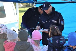 Na zdjęciu policjanci rozdający dzieciom kolorowanki.