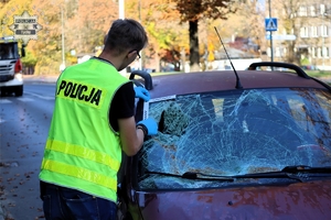 Na zdjęciu policjant w kamizelce odblaskowej przy samochodzie z rozbitą szybą przednią.