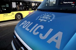 Na zdjęciu oznakowany radiowóz Policji. W tle autobus komunikacji miejskiej.