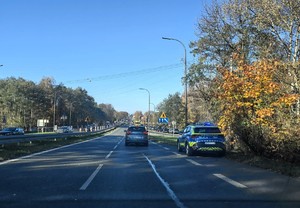 Na zdjęciu droga. Na poboczu zaparkowany radiowóz Policji.