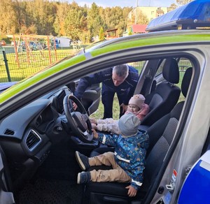 Na zdjęciu umundurowany policjant oraz dzieci siedzące w radiowozie.