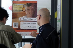 Na zdjęciu umundurowany policjant oraz kobieta zawieszający plakat kampanii