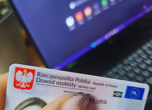 Na zdjęciu trzymany w dłoni dowód osobisty. W tle komputer