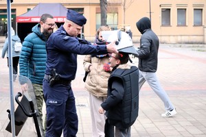 Na zdjęciu umundurowany policjant zakładający chłopcu policyjny kask