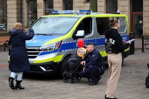 Na zdjęciu umundurowany policjant przy wózku z dzieckiem i kobieta robiąca zdjęcie