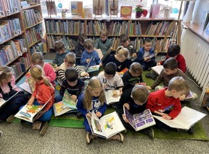 Na zdjęciu dzieci siedzące w bibliotece i oglądające książki