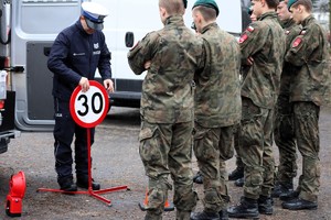 Na zdjęciu policjant ruchu drogowego oraz uczniowie klasy mundurowej stojący obok radiowozu