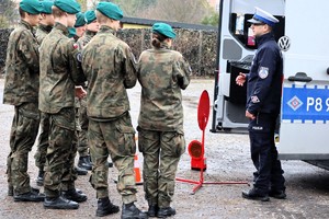 Na zdjęciu policjant ruchu drogowego oraz uczniowie klasy mundurowej stojący obok radiowozu