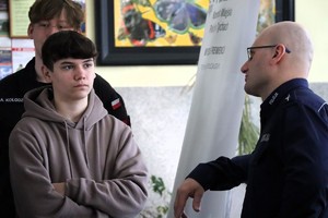 Na zdjęciu umundurowany policjant podczas rozmowy z uczniami biorącymi udział w dniu otwartym szkoły.