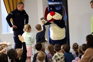 Na zdjęciu umundurowany policjant z policyjną maskotką Sznupkiem oraz grupą dzieci