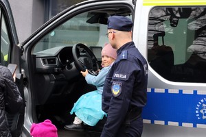 Na zdjęciu umundurowany policjant oraz dziewczynka siedząca za kierownicą radiowozu