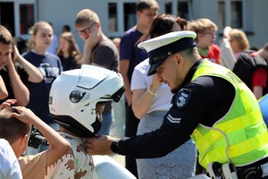Na zdjęciu policjant ruchu drogowego zakładający kask motocyklowy dziecku