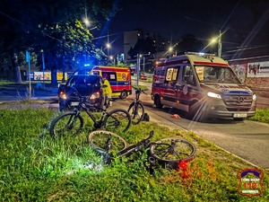 Na zdjęciu rowery stojące na trawniku. W tle karetki pogotowia