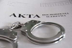 Zdjęcie przedstawiające kajdanki oraz teczkę z napisem akta dochodzenia/śledztwa