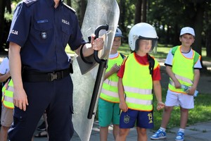 Na zdjęciu policjant trzymający tarczę, obok dzieci