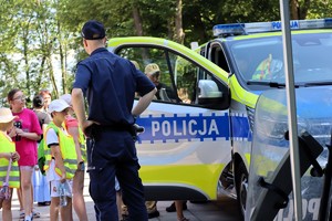 Na zdjęciu policjant z dziećmi. W tle radiowóz
