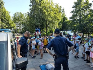 Na zdjęciu policjant i strażnik miejski przed grupą dzieci. W tle Sznupek