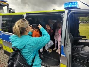 Na zdjęciu dzieci w radiowozie i kobieta robiąca im zdjęcie