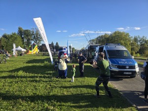 kolorowe zdjęcie przedstawiające radiowóz policyjny oraz Sznupka wraz z dziećmi i ich opiekunami