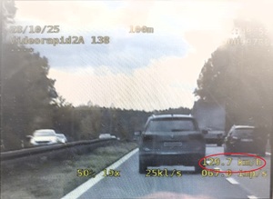 Kolorowe zdjęcie ekranu videorejestratora na którym widać fragment drogi krajowej z poruszającymi się po niej pojazdami. Na zdjęciu widnieją wskazania prędkości oraz czasu przeprowadzenia pomiaru.