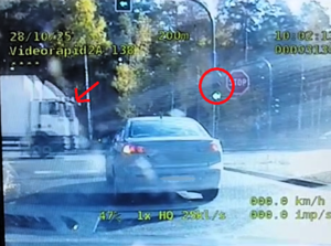 kolorowe zdjęcie ekranu videorejestratora radiowozu, na którym widoczne jest skrzyżowanie z sygnalizacją świetlną oraz przejeżdżający samochód ciężarowy. Na drodzę którą przecina kierowca samochodu ciężarowego wyświetla się światło koloru zielonego.