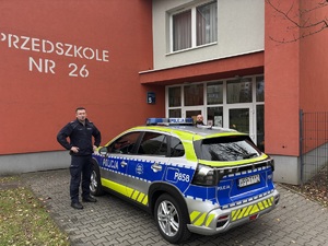 kolorowe zdjęcie umundurowanych policjantów oraz oznakowanego radiowozu przed budynkiem przedszkola numer 26 w Tychach.
