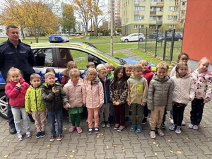 kolorowe zdjęcie dzieci z umundurowanym policjantem przed oznakowanym radiowozem.