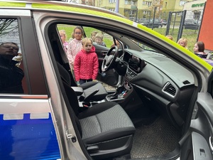 kolorowe zdjęcie dzieci stojących w świetle otwartych drzwi oznakowanego radiowozu