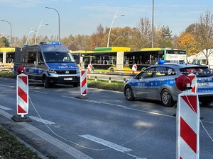 Kolorowe zdjęcie oznakowanych radiowozów. W tle widoczne są autobusy komunikacji miejskiej.