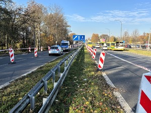 Kolorowe zdjęcie drogi w rejonie cmentarza. Widoczne są zaparkowane oznakowane radiowozy policji. Na drodze widoczny odbywający się ruch pieszych oraz pojazdów.