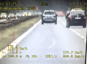 Kolorowe zdjęcie ekranu urządzenia rejestrującego prędkość, na którym widoczny jest fragment drogi oraz pojazd jadący nią, wraz ze wskazaniem wartości przekroczenia prędkości.