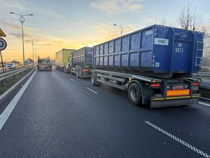 Kolorowe zdjęcie fragmentu drogi, na której stoją samochody uczestniczące w zdarzeniu drogowym - dwa pojazdy ciężarowe oraz samochód osobowy.