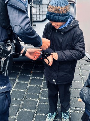 Kolorowe zdjęcie chłopczyka, któremu policjant prezentuje kajdanki policyjne.