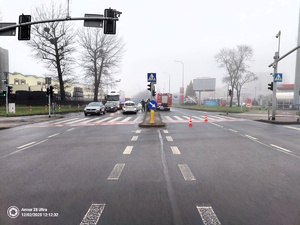 Kolorowe zdjęcie skrzyżowania z sygnalizacją świetlną, na którym widoczne są samochody uczestniczące w zdarzeniu drogowym, oznakowane pojazdy służb oraz umundurowani policjanci.