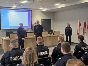 Kolorowe zdjęcie wykonane w sali konferencyjnej, na którym widać umundurowanych Komendantów Policji bielskiej oraz tyskie, przemawiających do umundurowanych policjantów.