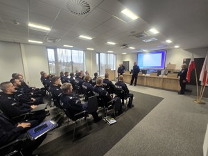 Kolorowe zdjęcie wykonane w sali konferencyjnej, na którym widać umundurowanych Komendantów Policji bielskiej oraz tyskie, przemawiających do umundurowanych policjantów.